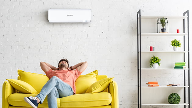 man sitting on couch underneath mistsubishi heavy industies air conditioner